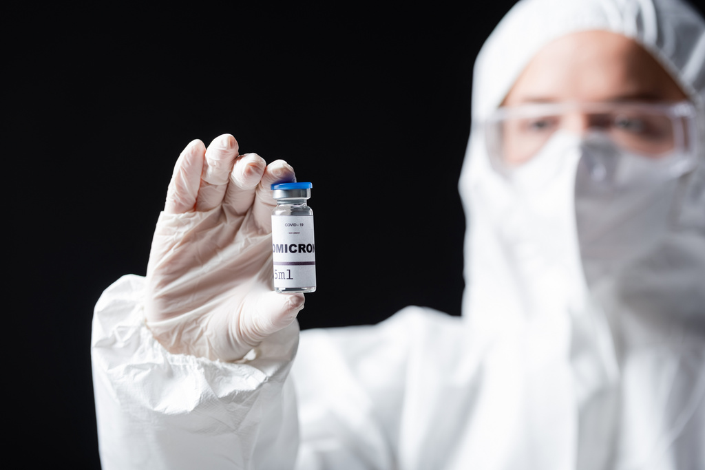 blurred immunologist in white hazmat suit holding covid-19 omicron variant vaccine isolated on black - Foto, afbeelding