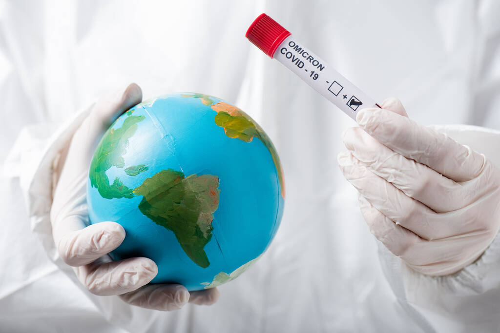 partial view of scientist in hazmat suit and latex gloves holding globe and positive covid-19 omicron variant test  - Zdjęcie, obraz