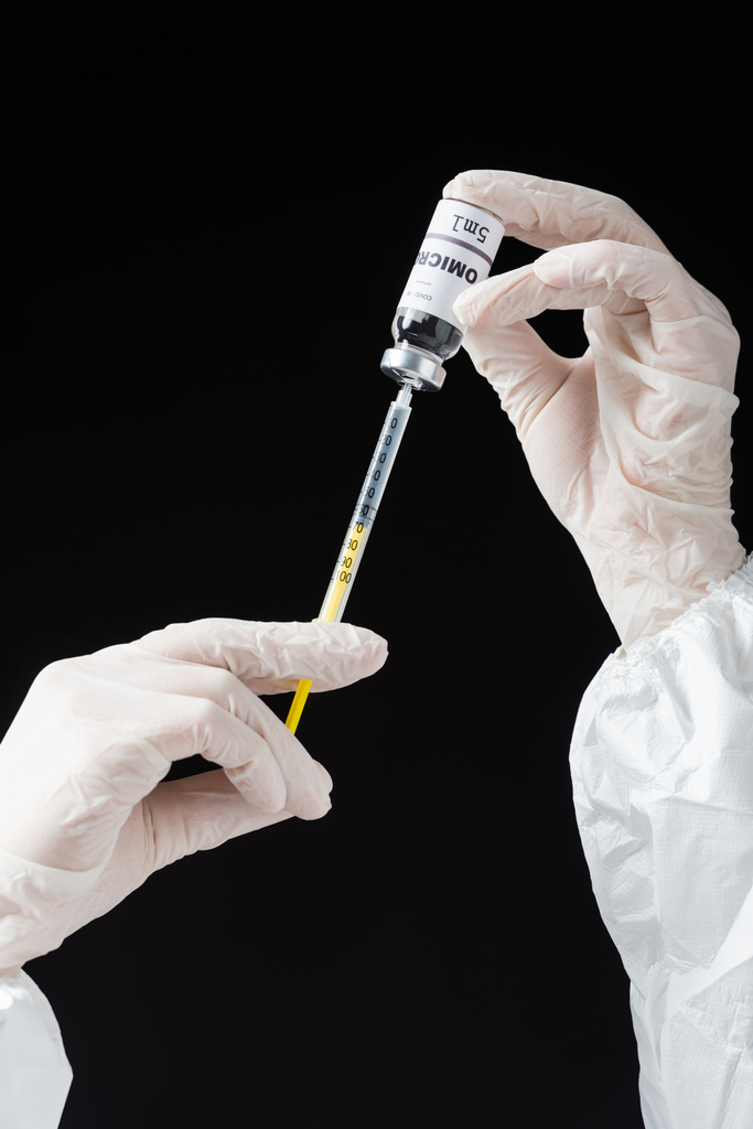 partial view of immunologist in white latex gloves holding syringe and omicron variant vaccine isolated on black - 写真・画像