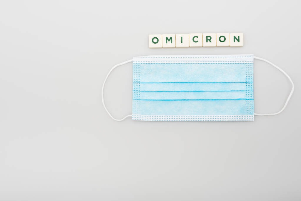 top view of medical mask near white cubes with omicron lettering on grey background - Valokuva, kuva