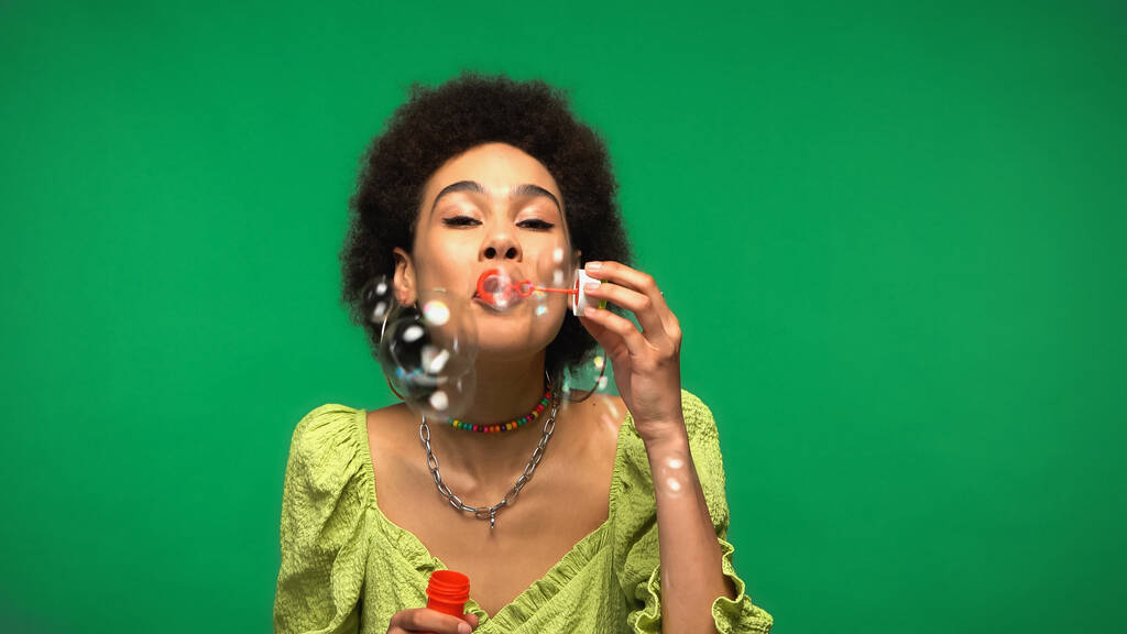 кучерява афроамериканська жінка дме мильні бульбашки ізольовані на зеленому
  - Фото, зображення