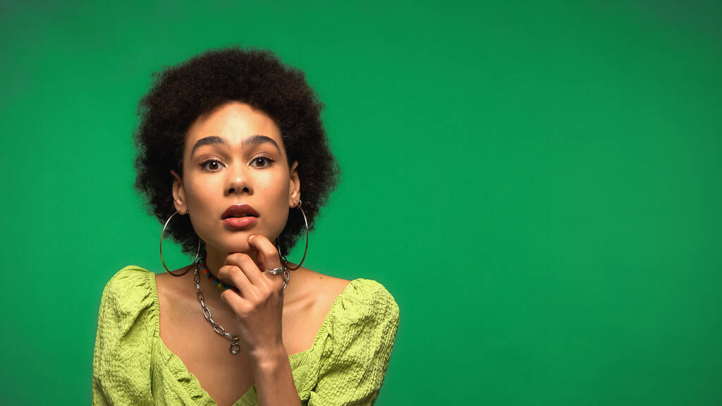 zamyšlená afro americká žena při pohledu na kameru izolované na zelené  - Fotografie, Obrázek