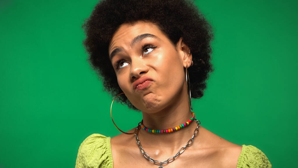 δυσαρεστήθηκε αφρικάνικη αμερικανίδα γυναίκα με σκουλαρίκια στεφάνης κοιτάζοντας μακριά απομονωμένη στο πράσινο  - Φωτογραφία, εικόνα