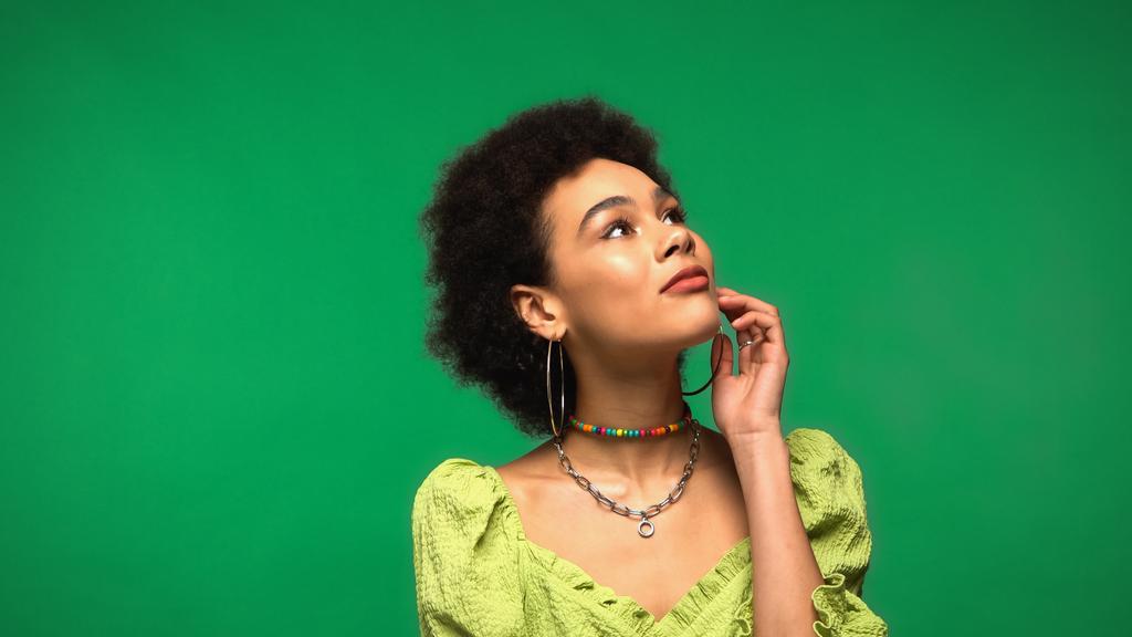 marzycielska Afroamerykanka w bluzce i kolczykach odwracając wzrok odizolowana na zielono - Zdjęcie, obraz