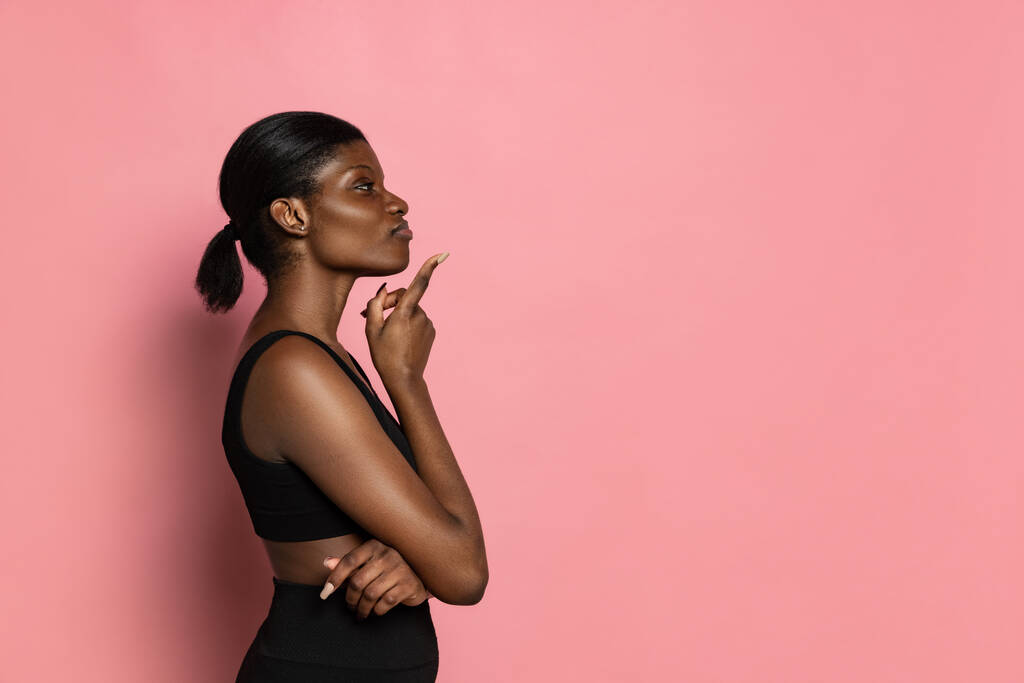 Profile view of young beautiful dark skinned woman izolowane na różowym tle studio z miejsca na reklamę. - Zdjęcie, obraz