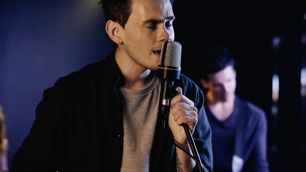 tattooed man singing in microphone near blurred musician on stage - Fotoğraf, Görsel