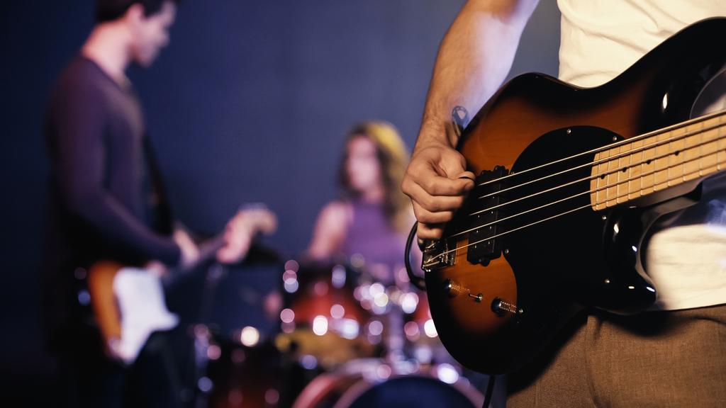 KYIV, UCRANIA - 30 DE DICIEMBRE DE 2021: vista recortada del guitarrista tatuado tocando con banda borrosa en el escenario  - Foto, Imagen
