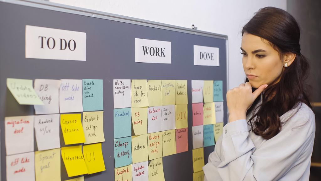 pensive businesswoman thinking near colorful sticky notes on board - Foto, afbeelding