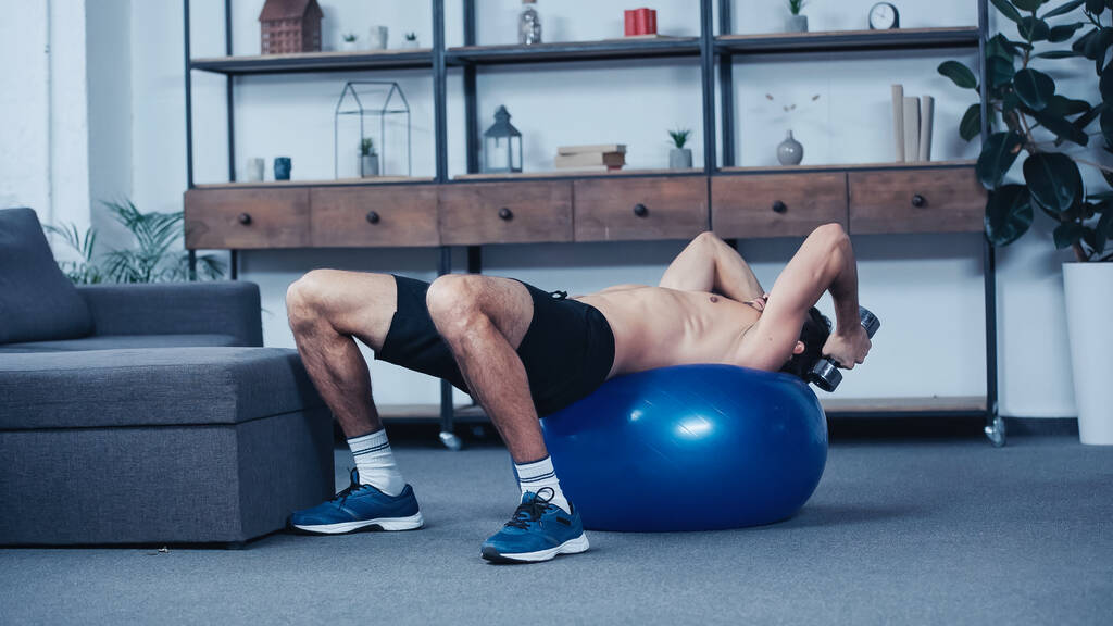 shirtless sportsman training with dumbbell on fitness ball at home  - Foto, Bild