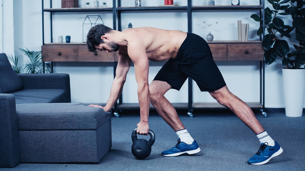 shirtless sportsman training with kettlebell near grey sofa  - Foto, immagini