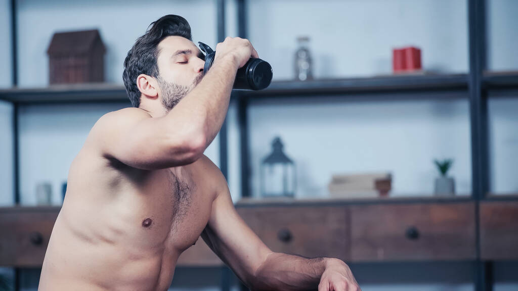μυώδης αθλητής κρατώντας αθλητικό μπουκάλι και πόσιμο νερό στο σπίτι - Φωτογραφία, εικόνα
