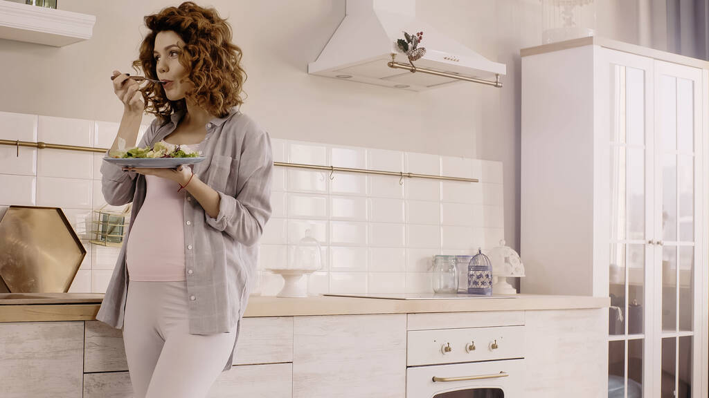 Mujer embarazada comiendo ensalada sabrosa y fresca en la cocina  - Foto, imagen