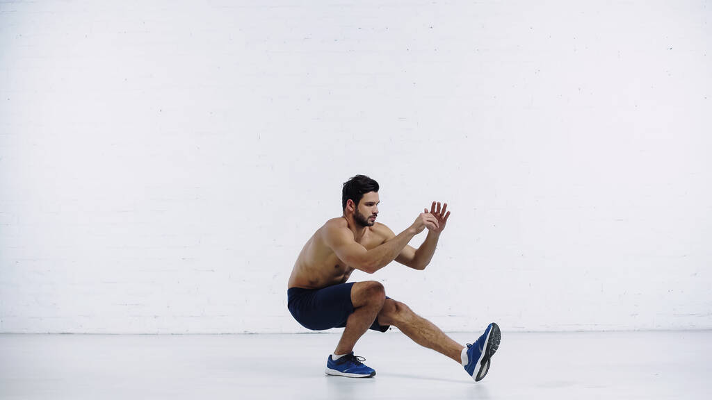 bearded sportsman in shorts and sneakers working out near white brick wall - Foto, immagini