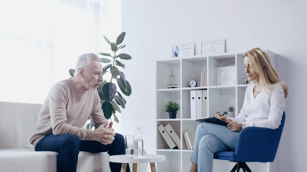 hombre maduro hablando con psicólogo con portapapeles en la sala de consulta  - Foto, imagen