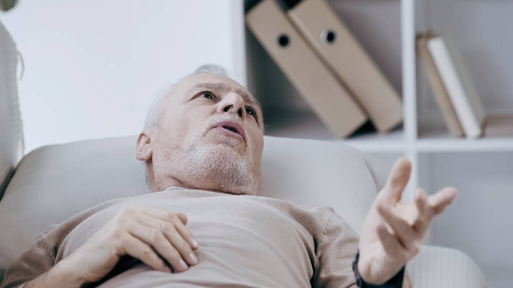 Orta yaşlı bunalımlı bir adam kanepeye uzanıyor ve danışma odasında konuşuyor. - Fotoğraf, Görsel