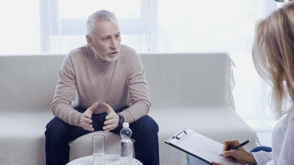 Keski-ikäinen mies istuu sohvalla ja puhuu psykoterapeutin kanssa  - Valokuva, kuva