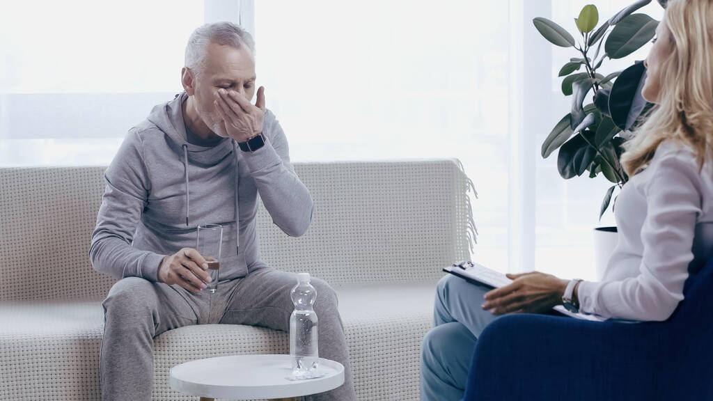 man van middelbare leeftijd in sportkleding het nemen van pil in de buurt van blonde psychotherapeut  - Foto, afbeelding