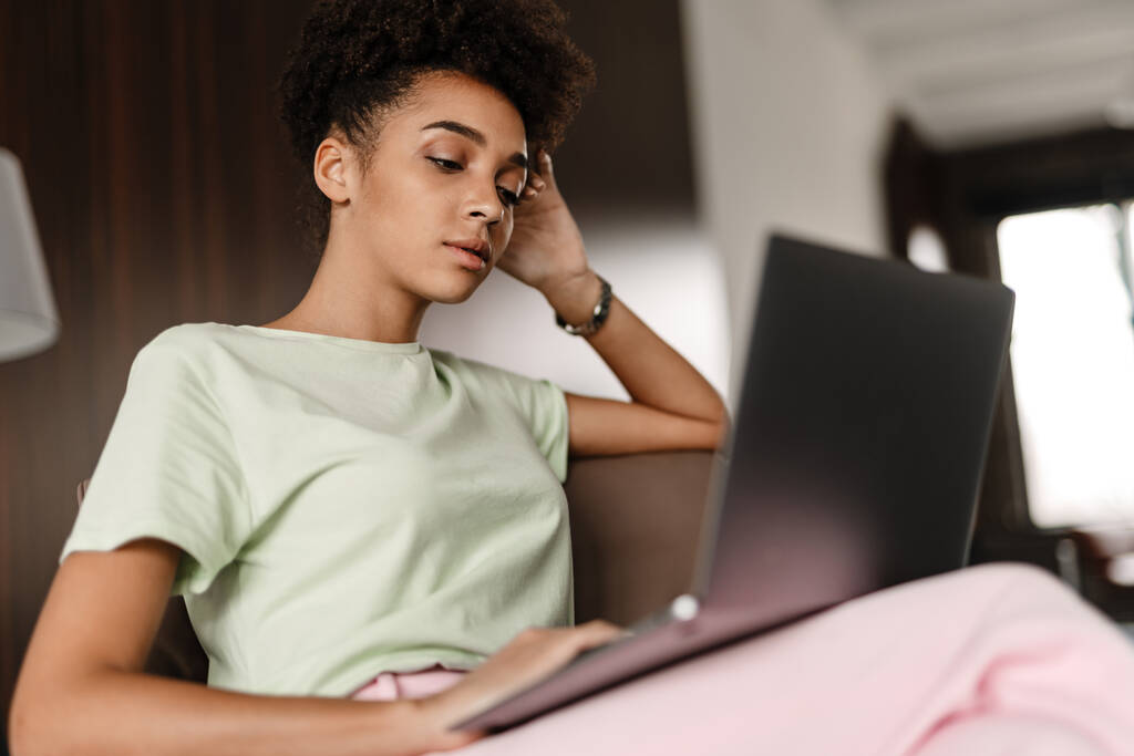若いです黒の女性作業ノートパソコンで座っている間アームチェアに自宅 - 写真・画像