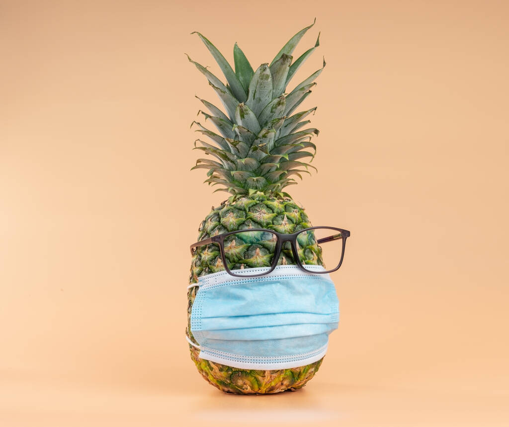 Interpretation of pineapple fruit in human form during a pandemic with glasses and a protective doctors mask. Copy space - 写真・画像