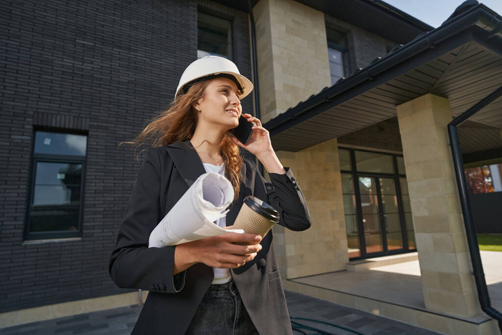 Female building engineer talking on smartphone near house - Photo, Image