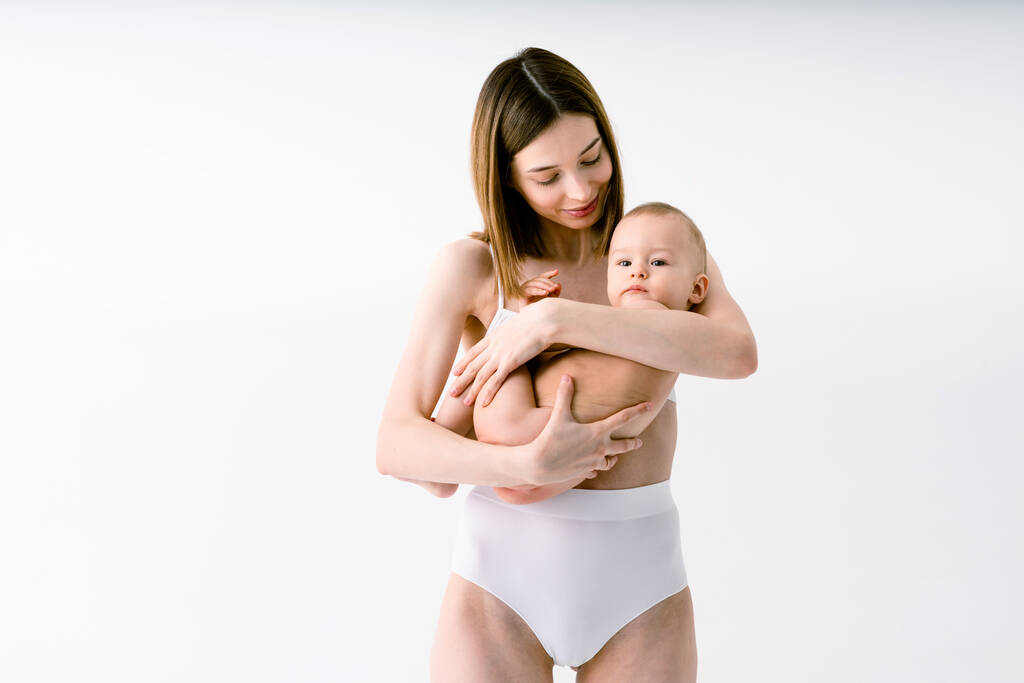 Femme heureuse tenant son bébé sur fond coloré - Jeune femme portant des sous-vêtements prenant soin de son petit fils - Grossesse, maternité, personnes et concept d'attente - Photo, image