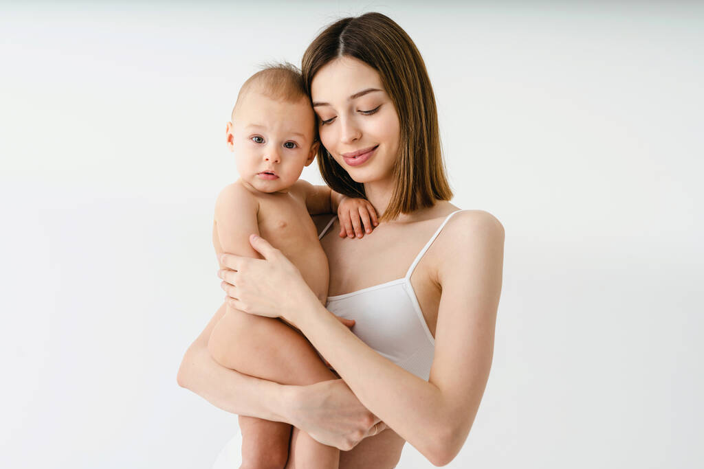 Ευτυχισμένη γυναίκα που κρατά το μωρό της σε έγχρωμο φόντο - Νεαρή γυναίκα που φοράει εσώρουχα που φροντίζει το μικρό γιο της - Εγκυμοσύνη, μητρότητα, τους ανθρώπους και την έννοια προσδοκία - Φωτογραφία, εικόνα
