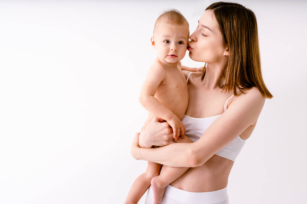 Mujer feliz sosteniendo a su bebé sobre un fondo de color - Mujer joven usando ropa interior cuidando a su pequeño hijo - Embarazo, maternidad, personas y concepto de expectativa - Foto, Imagen