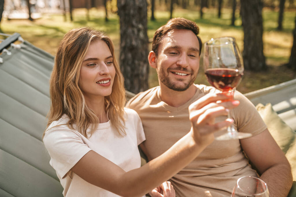 Młoda uśmiechnięta para trzyma kieliszki z winem i wygląda na szczęśliwą - Zdjęcie, obraz