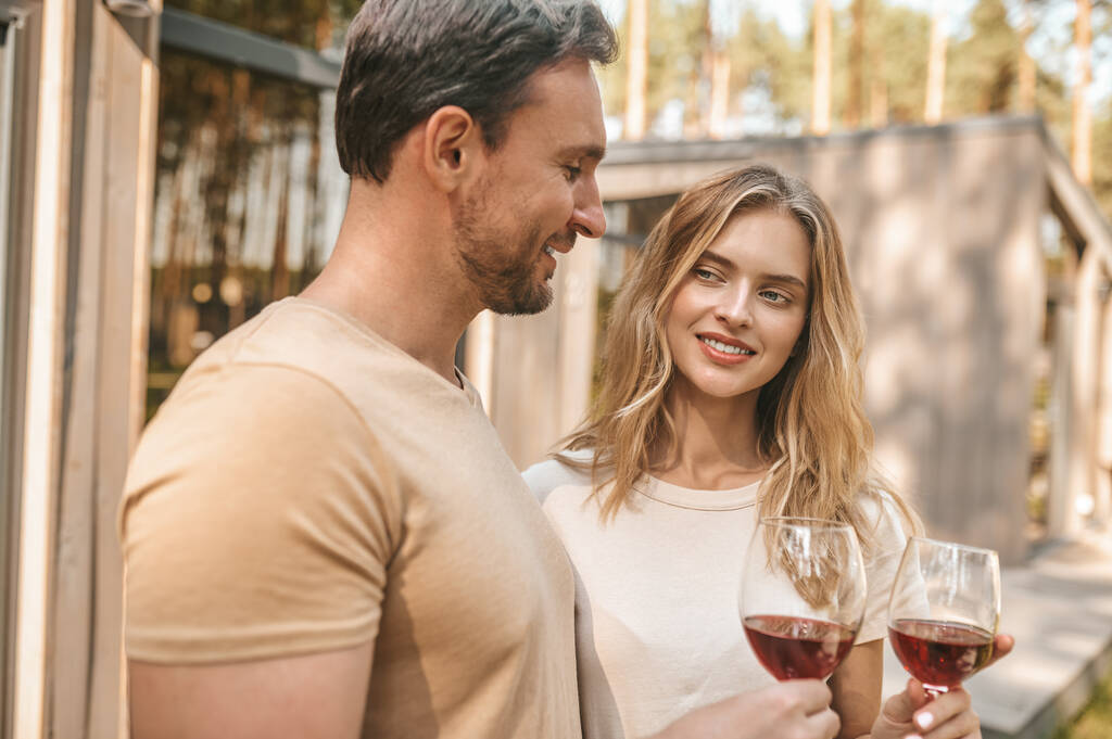Joven pareja sonriente sosteniendo vasos con vino y luciendo feliz - Foto, Imagen