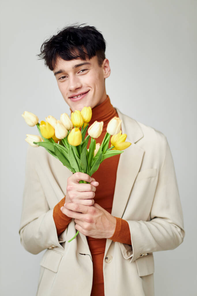 黄色の花の花束を持つ白いジャケットの美しい男エレガントなスタイルのモデルスタジオ - 写真・画像