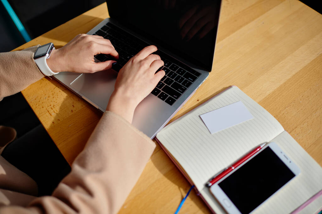 De cima, corte mulher anônima com relógio inteligente no laptop de navegação de pulso enquanto sentado na mesa de madeira com notebook e smartphone - Foto, Imagem
