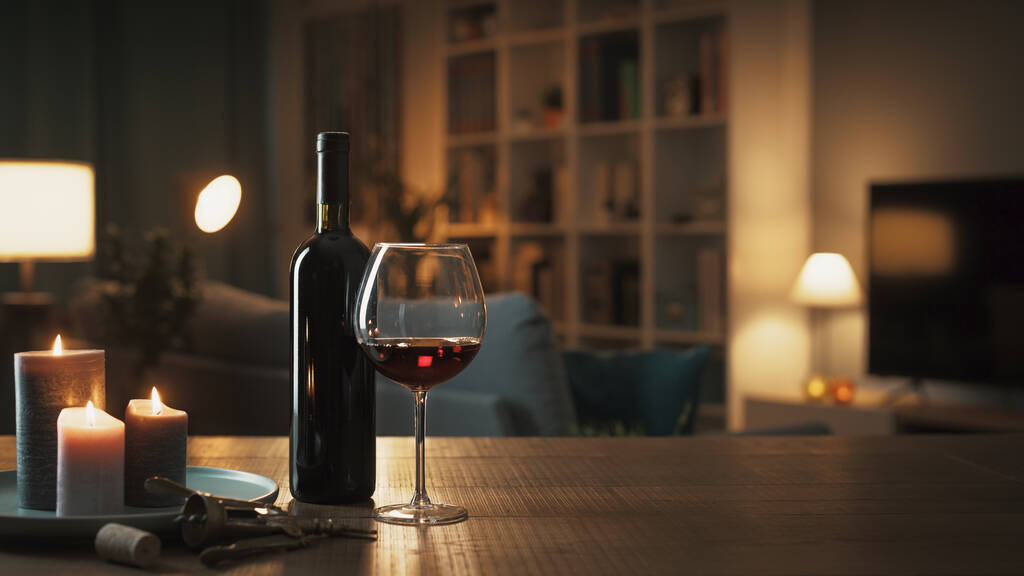 Degustacja czerwonego wina w domu: butelka wina, kieliszek do wina, korkociąg i świece na stole w salonie w nocy - Zdjęcie, obraz