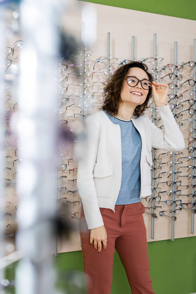 happy woman trying on eyeglasses in optics store on blurred foreground - Foto, Imagen