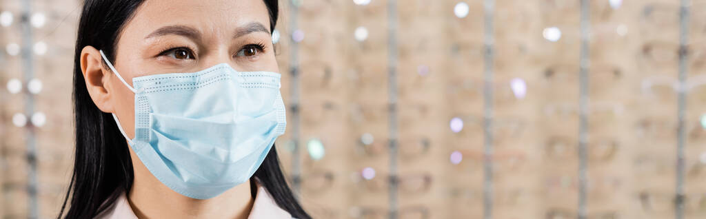asian ophthalmologist in medical mask in optics salon on blurred background, banner - Fotó, kép