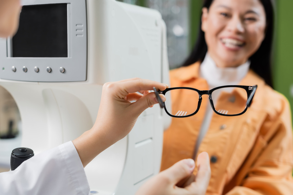 selective focus of eyeglasses in hand on oculist near vision screener and smiling asian woman - Foto, Imagem