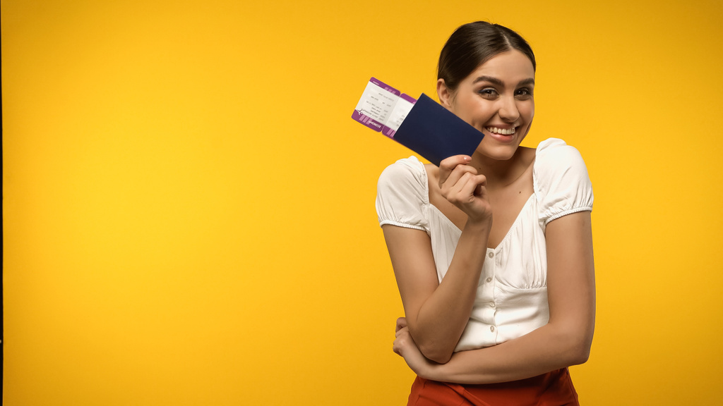 Cheerful tourist holding passport and boarding pass isolated on yellow - Photo, Image