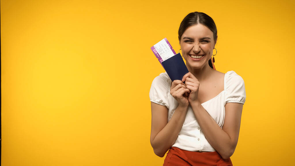 Excited traveler holding boarding pass and passport isolated on yellow - Fotografie, Obrázek