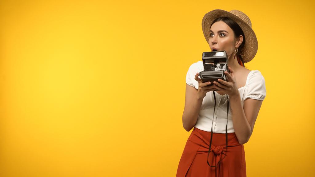 Excited tourist in straw hat holding vintage camera isolated on yellow - 写真・画像
