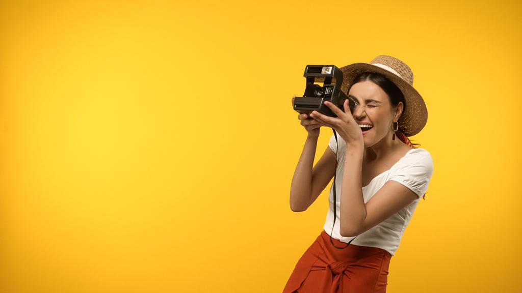 Excited tourist in blouse and sun hat taking photo on vintage camera isolated on yellow - Foto, Imagem