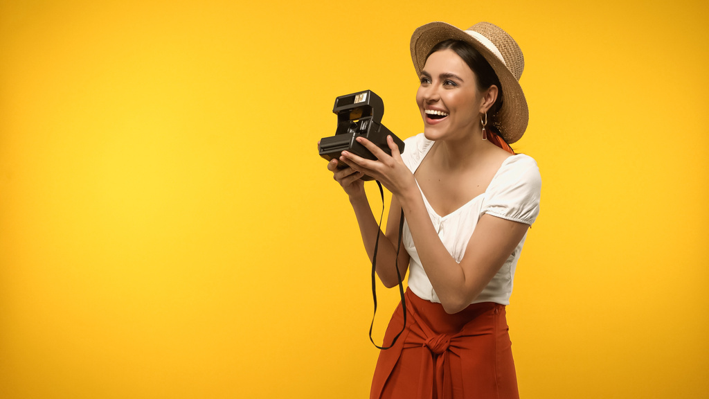 Szczęśliwa kobieta w słomkowym kapeluszu trzyma zabytkowy aparat fotograficzny i odwraca wzrok na żółto - Zdjęcie, obraz
