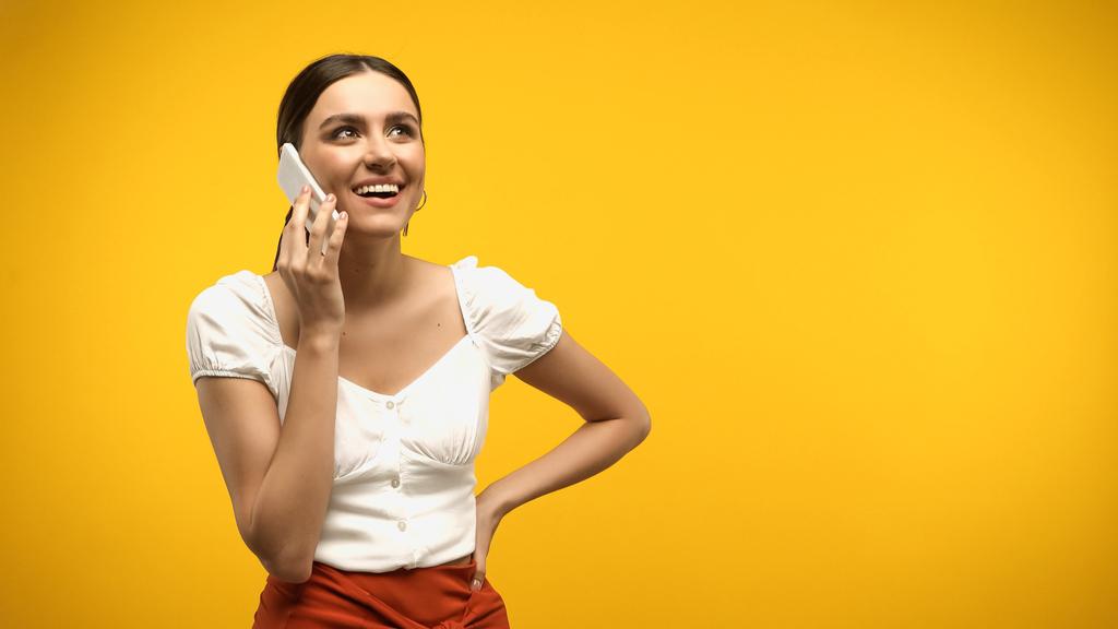 Bluz giymiş neşeli bir kadın cep telefonuyla konuşuyor, sarıda izole edilmiş.  - Fotoğraf, Görsel