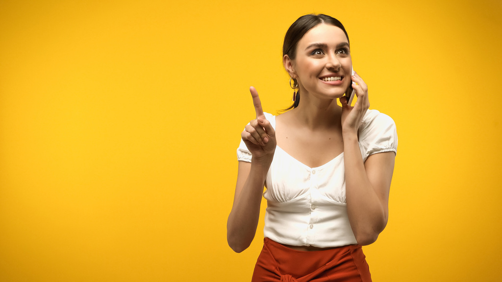 Young woman talking on smartphone and having idea isolated on yellow  - Photo, Image