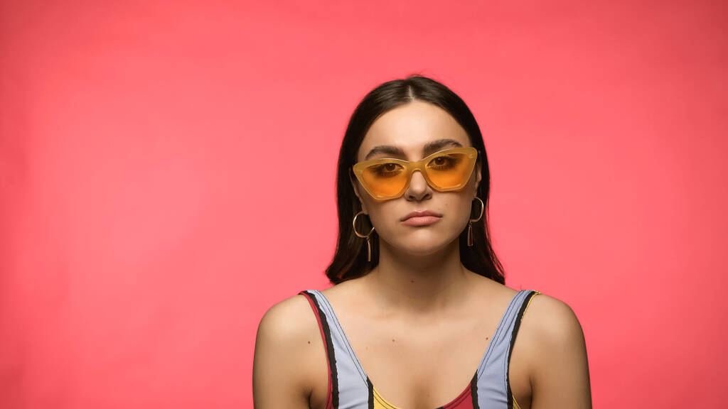 Sad woman in sunglasses and swimsuit looking at camera isolated on pink  - Photo, Image