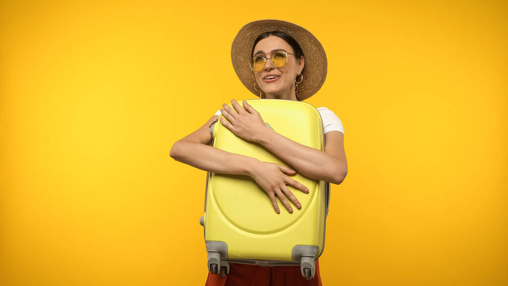Χαρούμενος τουριστικός κρατώντας βαλίτσα απομονωμένη στο κίτρινο  - Φωτογραφία, εικόνα
