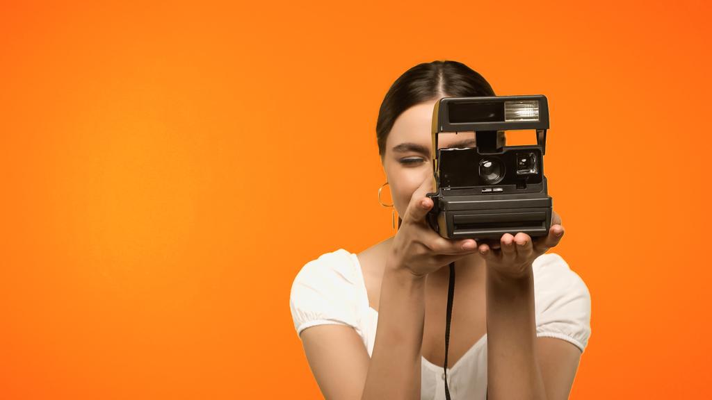Νεαρή γυναίκα τραβά φωτογραφία σε vintage κάμερα απομονωμένη σε πορτοκαλί  - Φωτογραφία, εικόνα