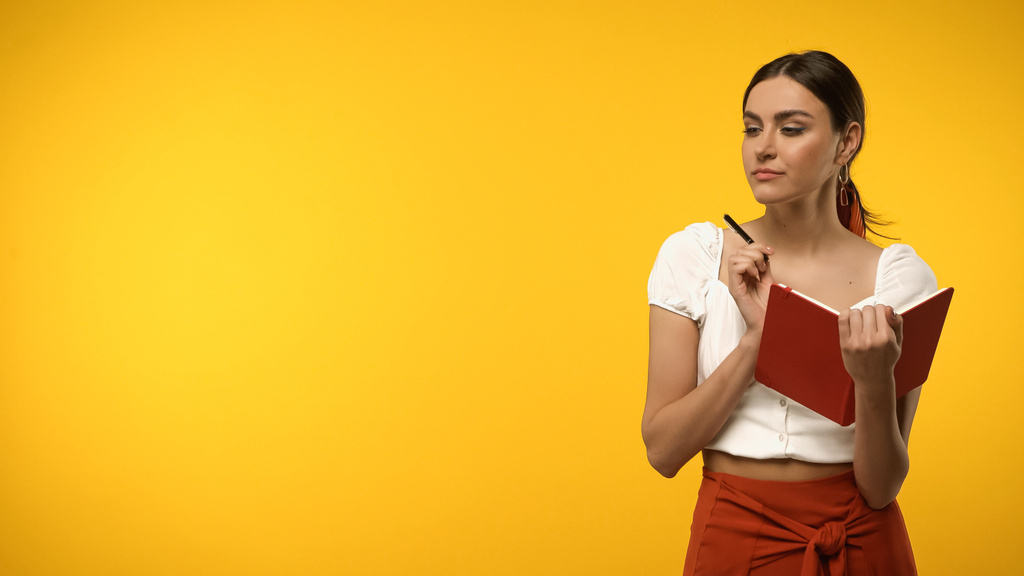 Young woman holding notebook and pen isolated on yellow - Фото, изображение