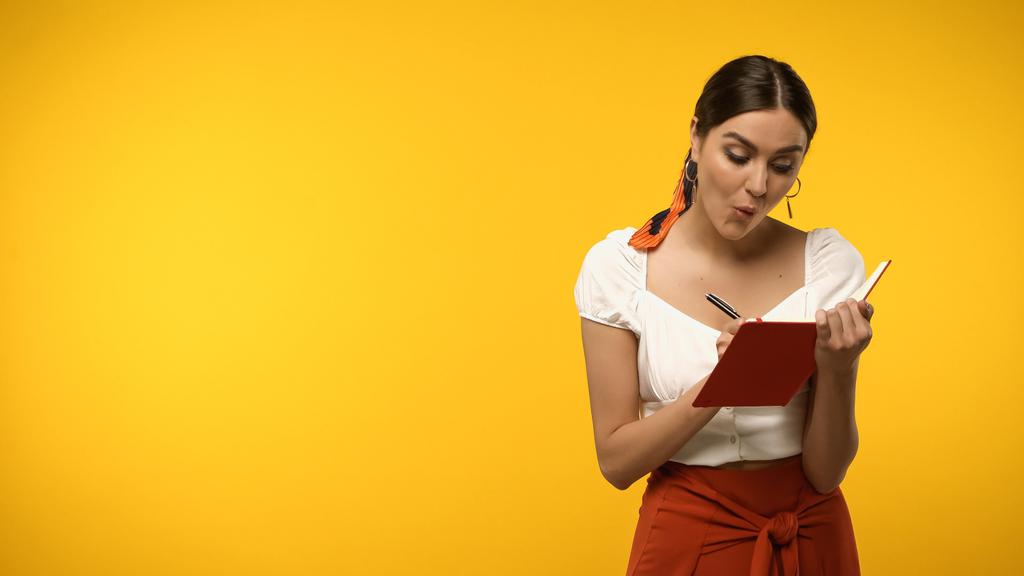 Geschokte vrouw schrijven op notebook geïsoleerd op geel - Foto, afbeelding