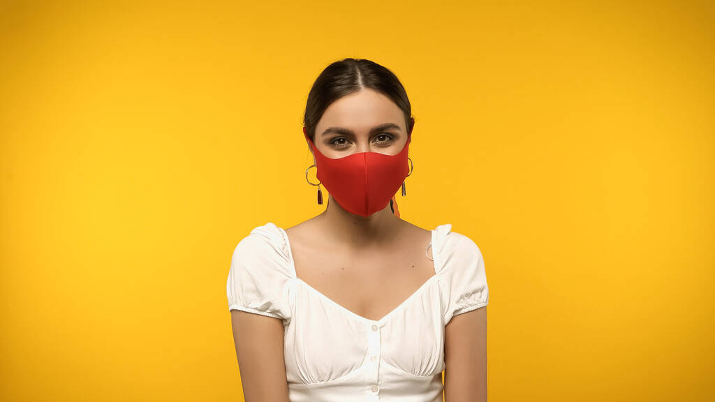 Fiatal nő védő maszkban nézi kamera elszigetelt sárga - Fotó, kép