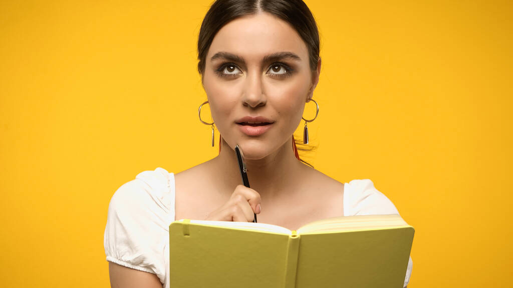 黄色に隔離されたノートブックの近くにペンを保持している女性 - 写真・画像