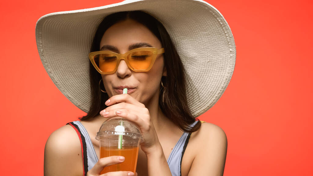 Pretty woman in sunglasses and swimsuit drinking cocktail isolated on coral  - Photo, image